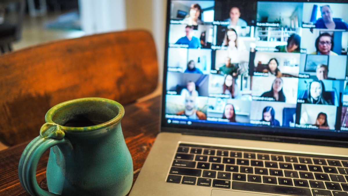 A laptop showing a remote team video call beside a coffee mug